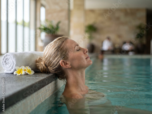 woman relaxing in spa pool with towel and flowers, peaceful and serene setting, close-up angle, stone tiles and waterproof material, white and blue tones, for relaxation.