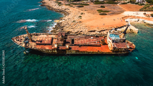 Obraz na plátně Wide aerial side view of a massive rusted shipwreck stranded in shallow waters