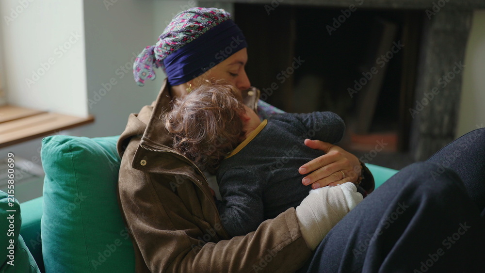Fototapeta premium Mother recovering from cancer embracing toddler on sofa at home, family support moment highlighting healing, resilience, attachment and emotional strength