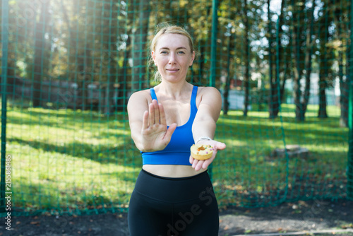 athletic woman holding donut dessert and showing refusal gesture,