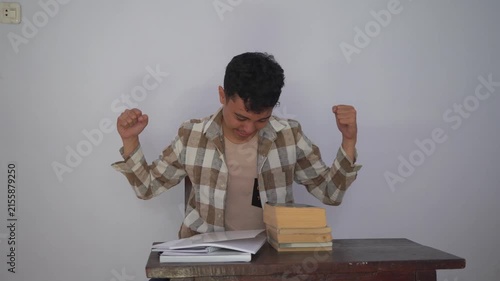 A Young Student Expressing Joy and Fatigue While Studying at a Wooden Desk with Books