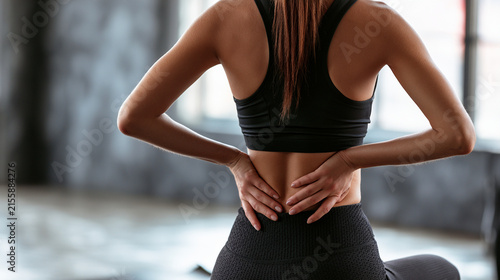 Woman suffering from back pain in gym, close up on hands on lower back
