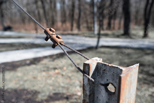 Close-up of a heavy duty steel cable with metal wire rope clamp fastened to a rusty iron beam outdoors.