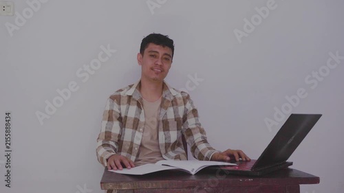 Engaging Young Man Working Alone at Desk with Laptop and Books in Minimalist Setting