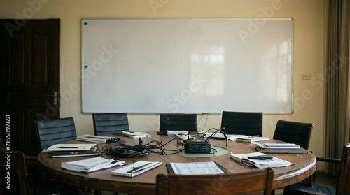 Round wooden meeting table with scattered notebooks and office equipment in a professional conference room setting