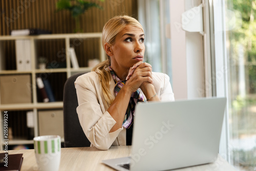 Bright small office with a thoughtful businesswoman contemplating at her desk