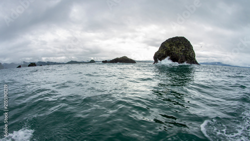 Wide angle view of rocky sea stacks and islets in the open ocean with waves crashing under a dramatic cloudy sky