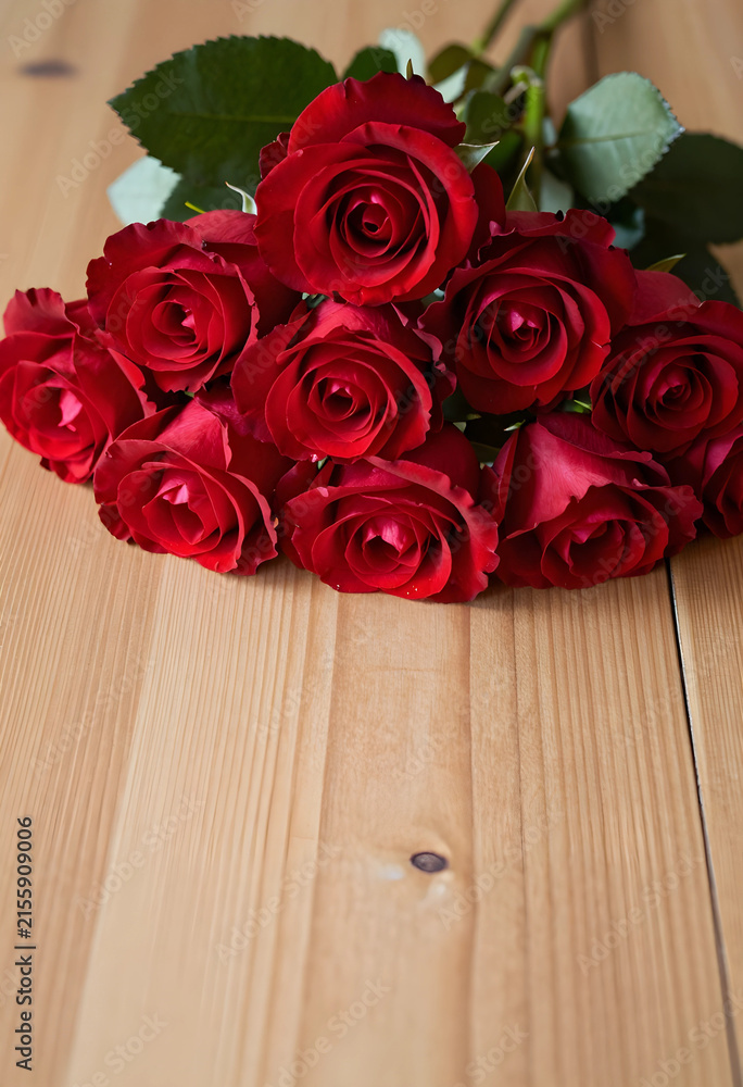 Fototapeta premium Bouquet of fresh red roses with green leaves on a light wooden table, romantic floral gift for special occasions