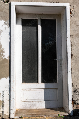 Vertical image, white door with glass on an abandoned industrial building.
