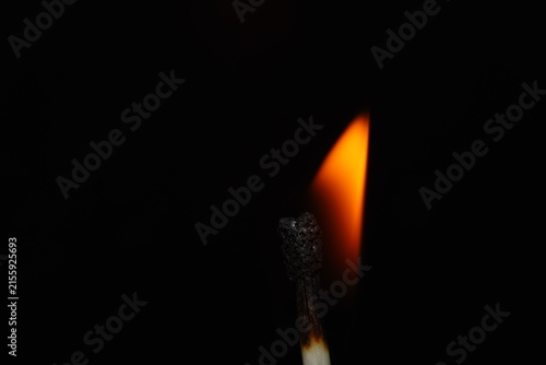 Minimal macro photograph of a burning match with a curved orange flame against a dark black background and generous copy space.