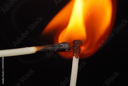 Dramatic macro image of a burning matchstick with an orange flame rising behind it against a dark background.