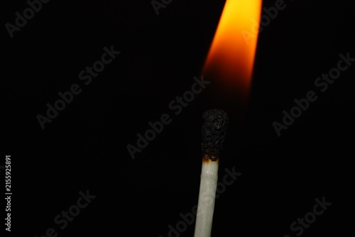 Moody close-up photograph of a blackened matchstick with a soft orange flame illuminating the darkness behind it.