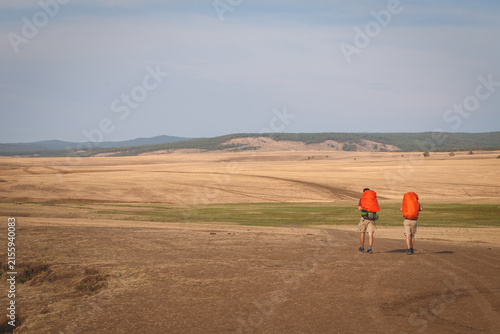 Two hikers with backpacks walking on trail against hills on Olkhon Island, Lake Baikal, Siberia