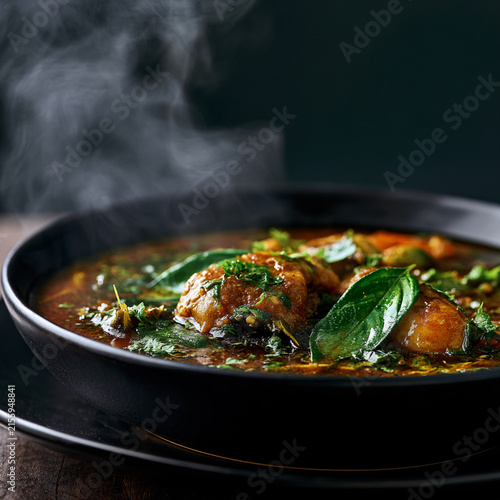 A steaming bowl of flavorful soup garnished with fresh herbs and greens.