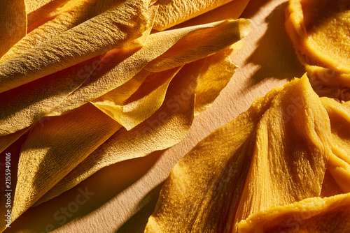 Close-up of vibrant yellow dried mango slices on a wooden surface, showcasing textures.