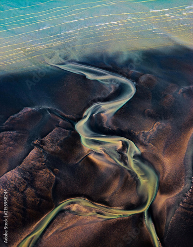 Dramatic aerial landscape with a winding river cutting through rugged dark terrain, creating organic natural patterns ideal for travel, geography, environmental and abstract landscape concepts.