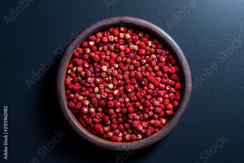 Fresh wild strawberries in a rustic clay bowl, closeup. Top view of round ceramic dish filled with large amount of ripe red forest wild strawberries placed on dark background with shadows
