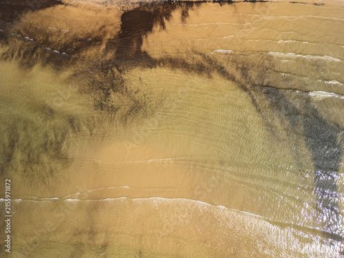 Albania, Durres 07 09 2025: Minimalist top-down drone photo of empty crystal clear shallow water with gentle waves, dark yellow sand, and underwater vegetation.