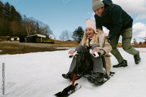 Father pushing daughter on snow sled.