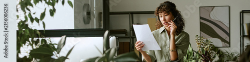 Header of Biracial young adult woman working in call center wearing headset and reading document. Image suitable for customer service training, and telemarketing campaigns