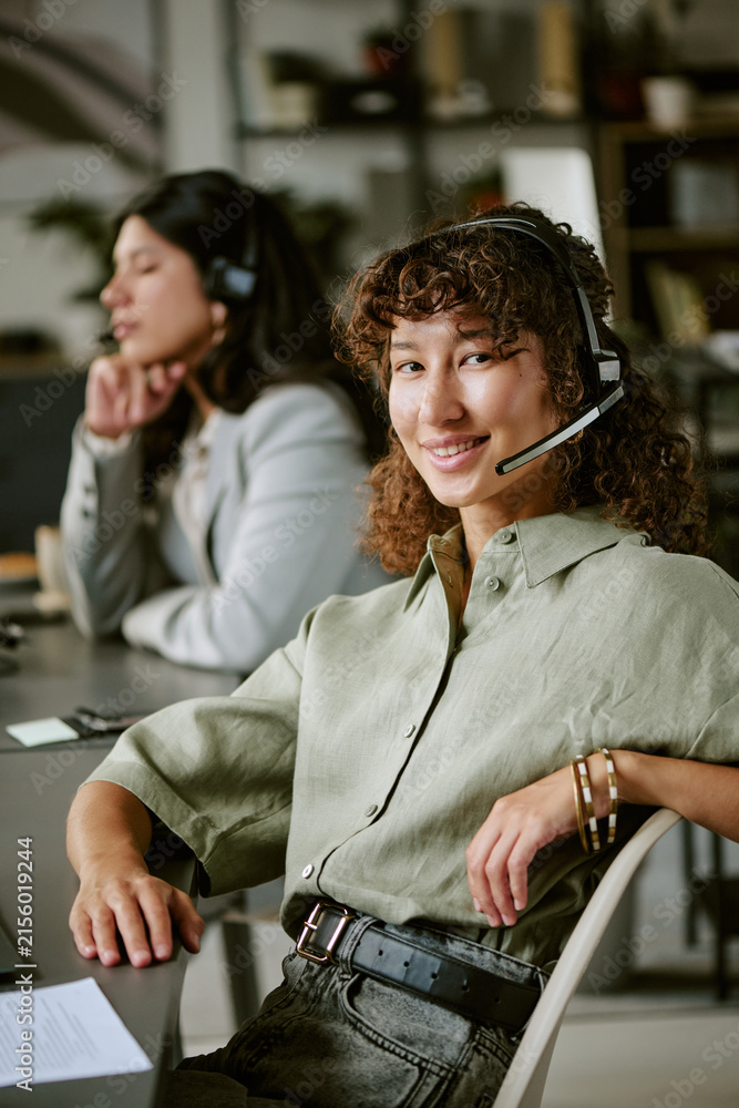 Fototapeta premium Portrait of diverse young adult female call center agents working in office wearing headsets. Image suitable for customer service training and corporate communication, vertical