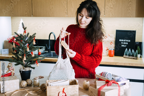Cuadro en lienzo Woman holds mesh bag and wooden brush over gift basket in kitchen near CHRISTMAS VIBES ONLY sign
