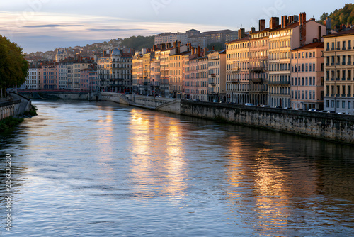 Golden hour illuminates historic architecture lining a serene urban river, with warm reflections dancing on the water surface.