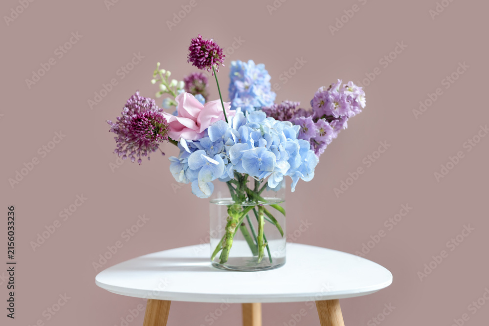 Obraz premium Bouquet of beautiful flowers in vase on white table near beige wall indoors, closeup
