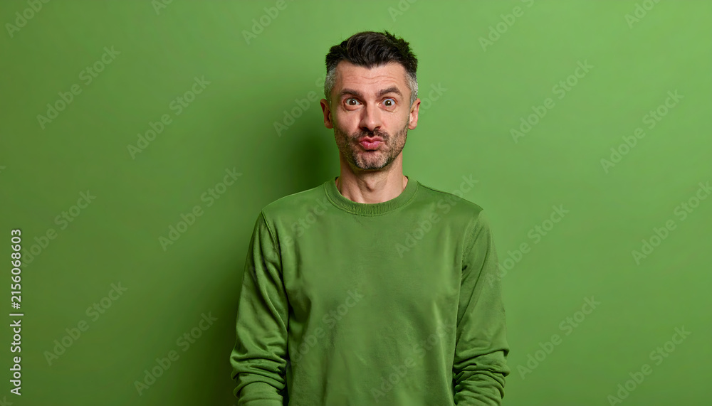Fototapeta premium Mature man stands making silly faces wearing forest green sweater for outdoor brand advertising generative AI