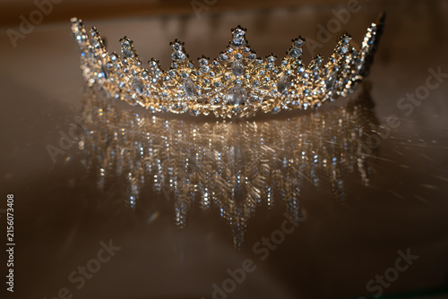 Luxury Golden Crown, diadem on Glass with Sparkling Light Reflections. on Beige Fabric Background.
