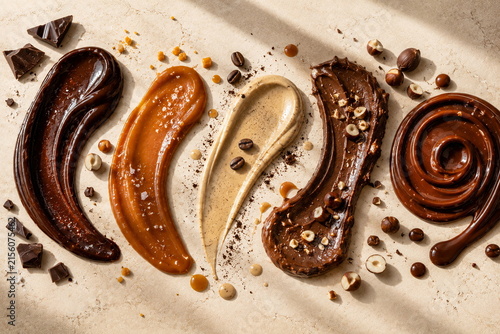 Indulgent assortment of chocolate, caramel, coffee and hazelnut spreads arranged artistically on a warm textured surface.