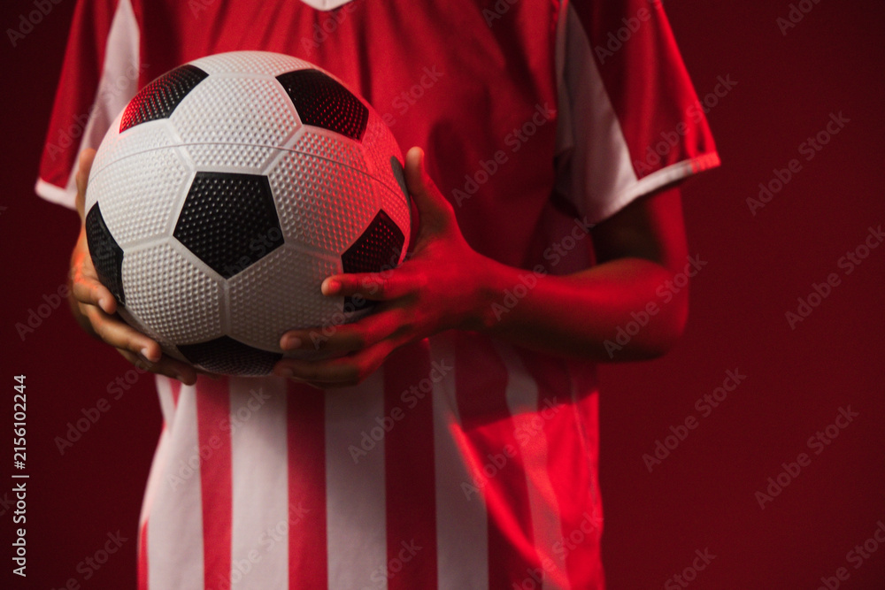 Fototapeta premium African American female holding black-white soccer ball in red-white jersey in red-lit studio
