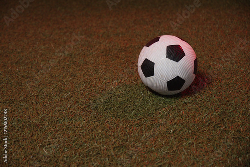 soccer ball is resting on short turf slightly right of center, showing red-tinted highlight