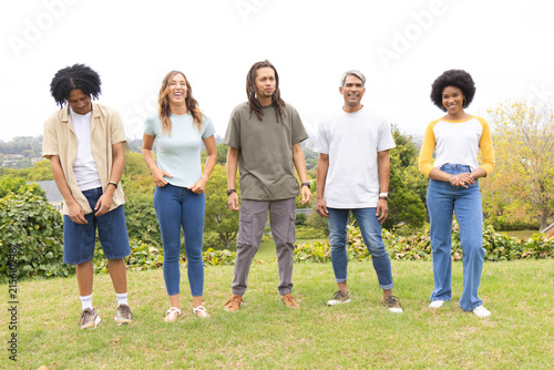 Diverse friends standing side-by-side on grassy slope in suburban park, wearing casual clothing