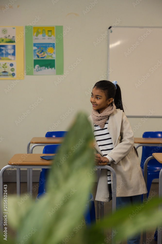 Obraz premium African American schoolgirl standing by wooden desks in classroom near potted plant, copy space