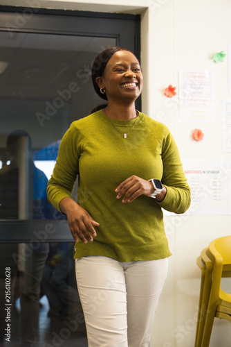 Adult African woman walking in classroom, speaking near glass door with posters and yellow chairs