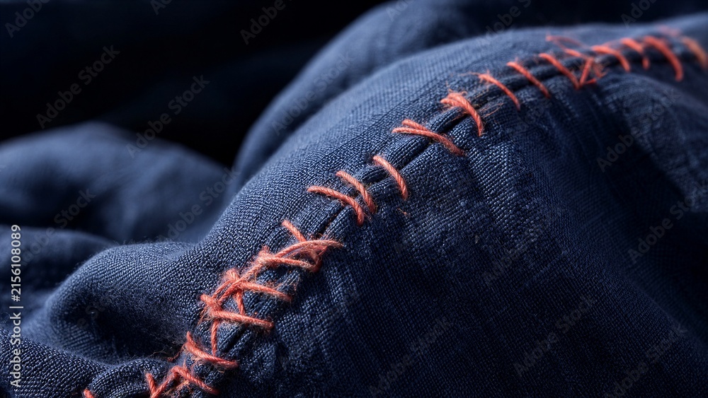 Fototapeta premium Close up view of blue fabric with orange hand stitching. Concept of garment repair, mending, and textile restoration.