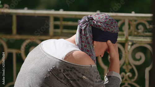 Woman undergoing chemotherapy sitting on balcony with head in hand, contemplative moment reflecting emotional burden, resilience, uncertainty and personal recovery journey