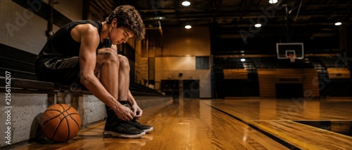 Young basketball player tying his shoes on the bench before a game