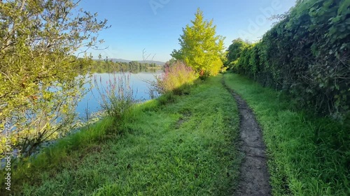 Dirt path curving along riverbank beside green vegetation