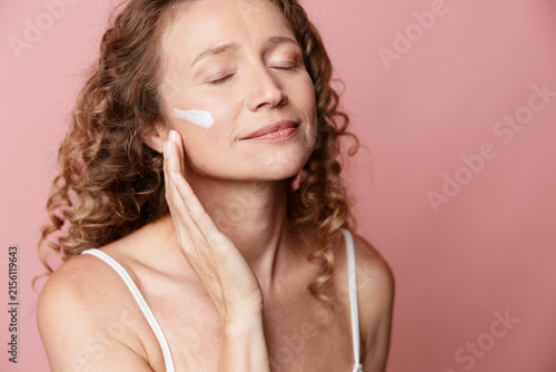Obraz na plátne An authentic middle aged woman applies cream to her face