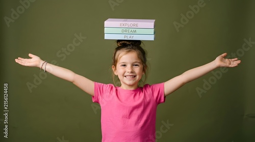 Young girl balancing books on head with arms outstretched for focus and posture exercise