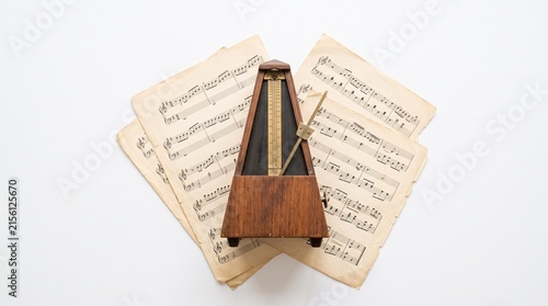 Metronome on Sheet Music: A vintage wooden metronome stands on a stack of aged sheet music, symbolizing rhythm, timing, and musical practice.