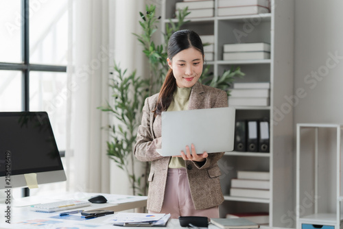 Bild auf Leinwand Focused Professional: A diligent businesswoman stands at her desk, intently focused on her laptop, surrounded by the organized clutter of a modern office