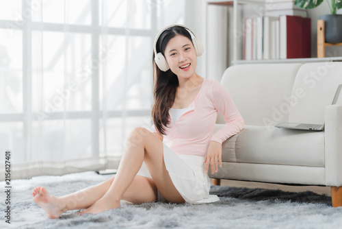 Konstfotografi Relaxing with Music: A young Asian woman with headphones enjoys music while sitting on the floor at home, a laptop nearby, showcasing a moment of leisure and personal enjoyment