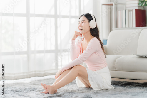 Quadro su tela Young Woman Listening to Music: A happy young woman with headphones enjoys her favorite tunes while sitting on the floor in a bright, sunlit room, lost in a moment of relaxation and personal bliss