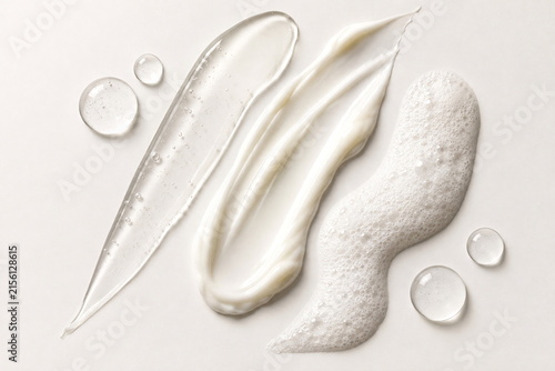 Luxury skincare cosmetic textures arranged in minimalist artistic compositions on a clean ivory background, featuring creamy lotions, translucent gels, foamy cleansers, glossy serum swatches, bubbles 