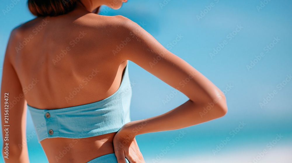 Fototapeta premium rear view of a woman model posing in swimwear on a bright tropical beach for a photoshoot with a friend photographer, back to camera, fashion travel concept, style, vacation,