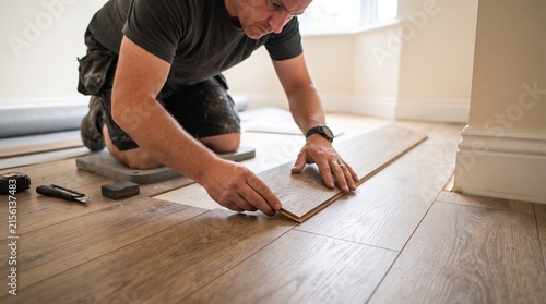 A skilled craftsman meticulously installs a new laminate wood floor, demonstrating precision and dedication in his work.