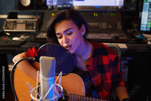Young woman with guitar singing in a recording studio